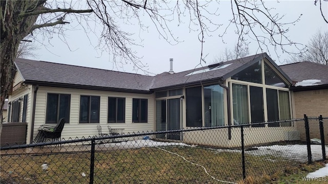 view of side of home with a fenced front yard, a sunroom, and a shingled roof