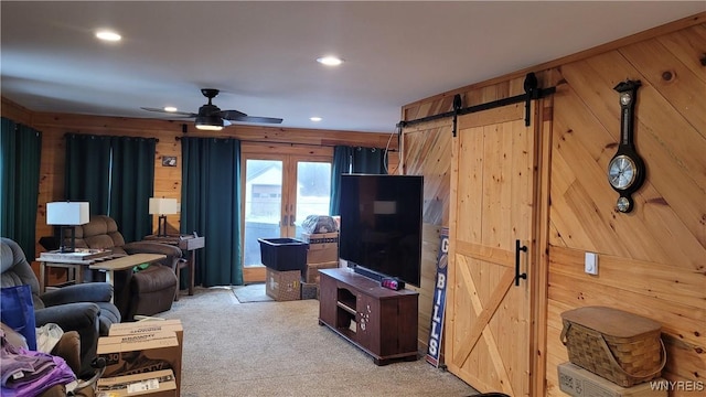 living area with a barn door, wooden walls, a ceiling fan, light colored carpet, and recessed lighting