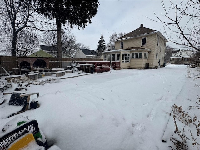 snow covered back of property featuring an outdoor fire pit, a sunroom, and fence