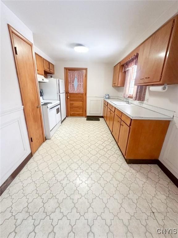 kitchen featuring electric range, brown cabinets, under cabinet range hood, light countertops, and light floors