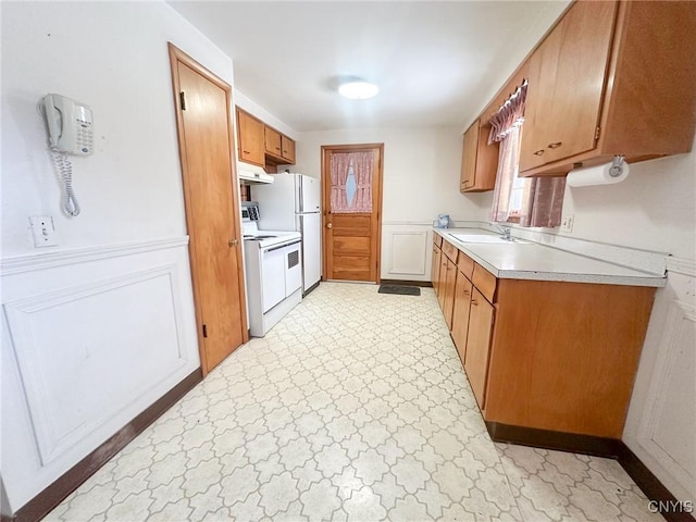 kitchen featuring light floors, light countertops, brown cabinetry, white appliances, and under cabinet range hood