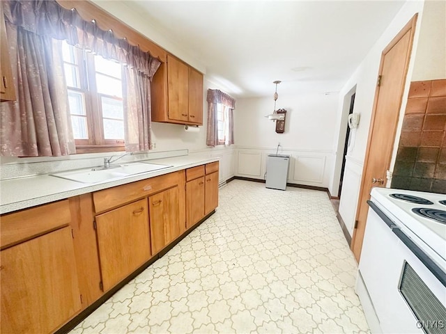 kitchen featuring electric stove, brown cabinets, light countertops, wainscoting, and a sink