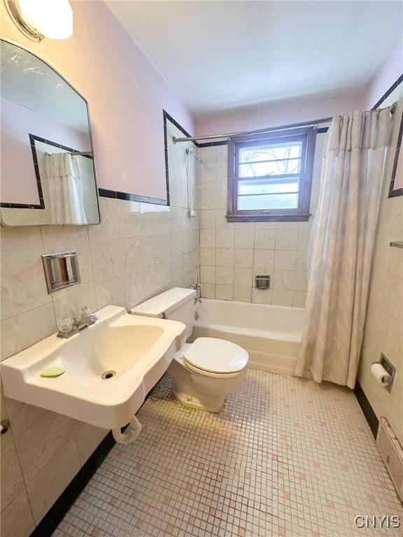 bathroom with tile walls, toilet, shower / bath combo, a sink, and tile patterned flooring