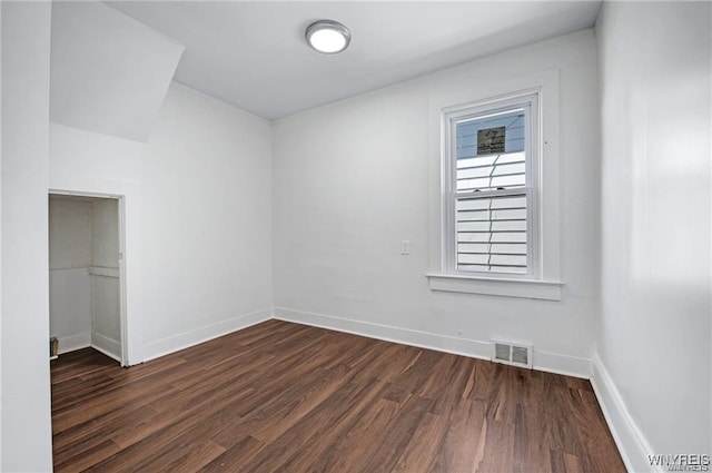 spare room with dark wood-style flooring, visible vents, and baseboards