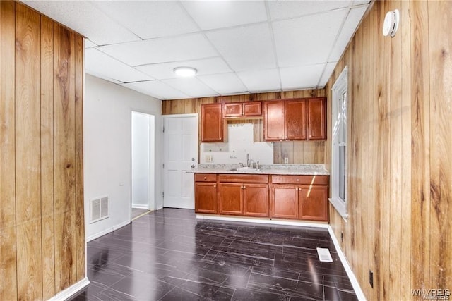 kitchen featuring visible vents, brown cabinets, light countertops, wood walls, and a sink