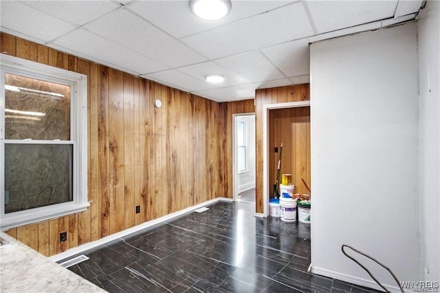 spare room with visible vents, wood walls, a drop ceiling, and baseboards