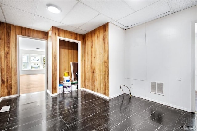 spare room with wood walls, visible vents, and a drop ceiling