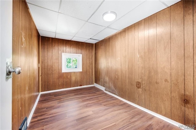 unfurnished room featuring a paneled ceiling, wood walls, wood finished floors, visible vents, and baseboards