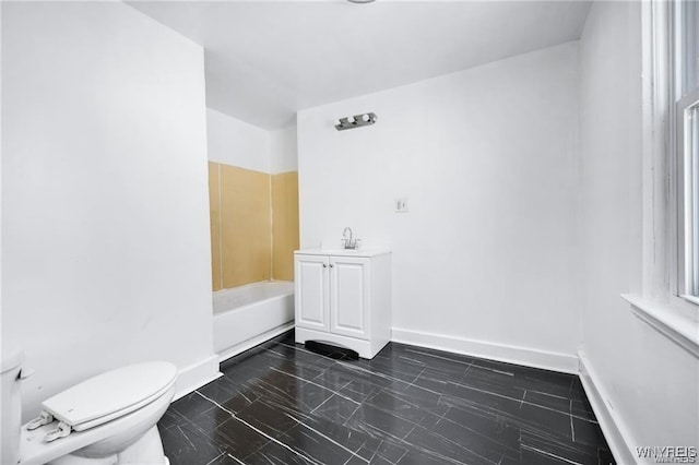 bathroom featuring toilet, a tub, baseboards, and a sink