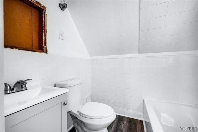 full bath with toilet, lofted ceiling, a bathtub, vanity, and tile walls