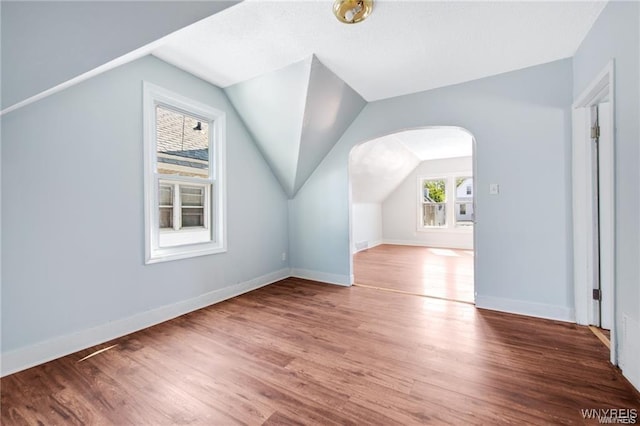 additional living space with lofted ceiling, arched walkways, wood finished floors, and baseboards