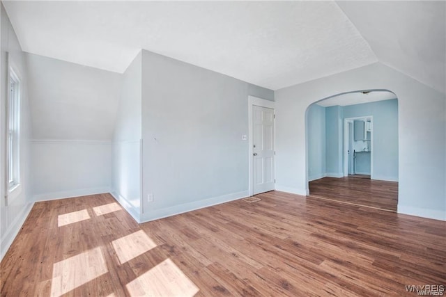 interior space featuring arched walkways, lofted ceiling, baseboards, and wood finished floors