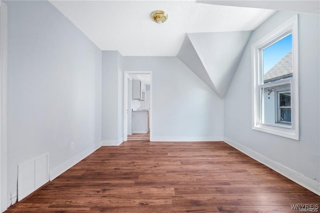 additional living space with vaulted ceiling, wood finished floors, visible vents, and baseboards