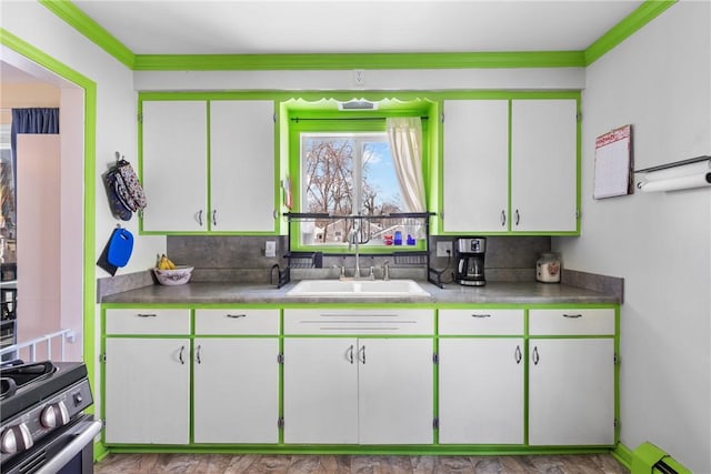 kitchen featuring a baseboard radiator, light countertops, ornamental molding, a sink, and gas range