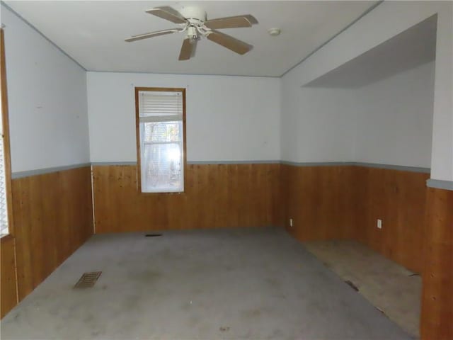 empty room featuring wainscoting, wood walls, and ceiling fan