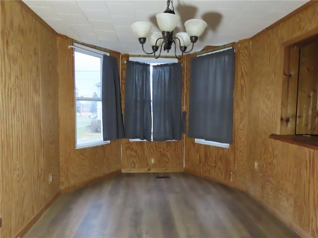 spare room with wood walls, a notable chandelier, baseboards, and wood finished floors