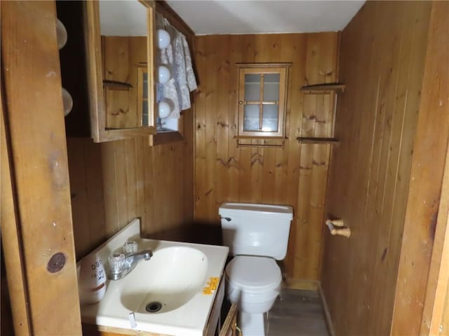 half bath with wood walls, vanity, and toilet