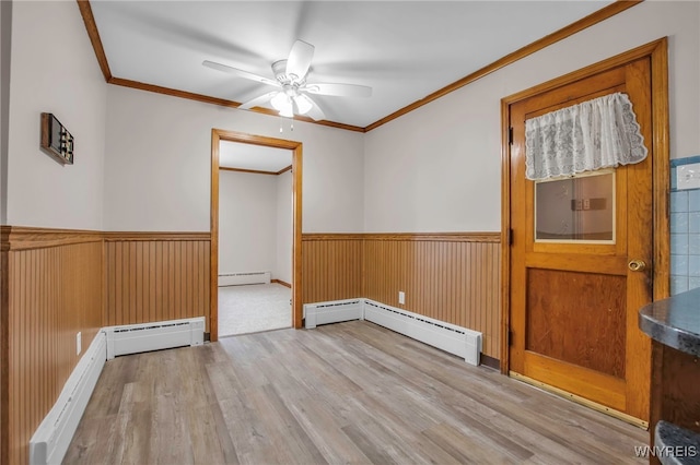 unfurnished room with baseboard heating, wainscoting, and crown molding