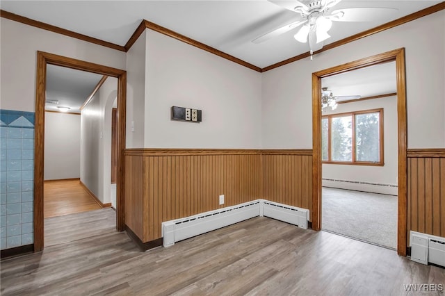 empty room with a baseboard heating unit, ornamental molding, wainscoting, and wood finished floors