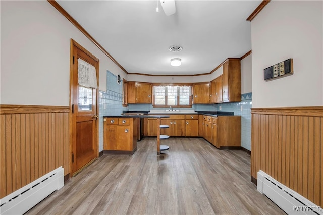 kitchen featuring a baseboard heating unit, brown cabinetry, wainscoting, and visible vents