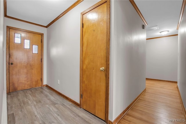 corridor featuring light wood finished floors, baseboards, and crown molding