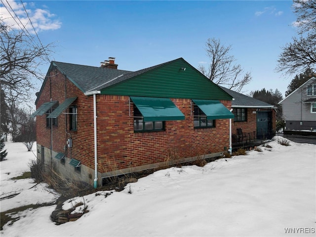 snow covered property with a chimney and brick siding