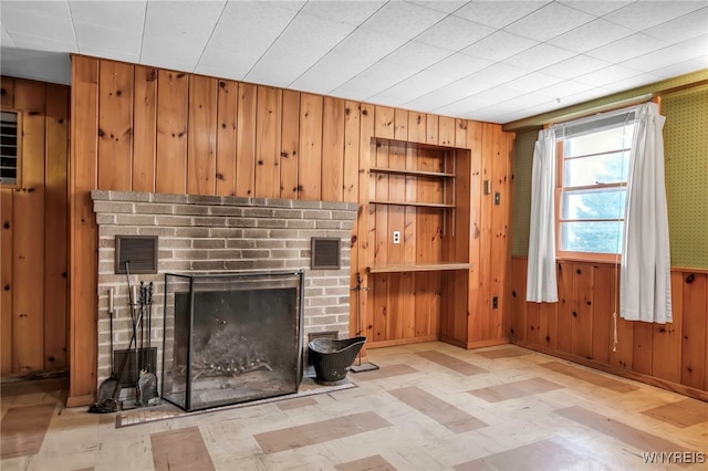 unfurnished living room with built in shelves, wooden walls, visible vents, and a fireplace