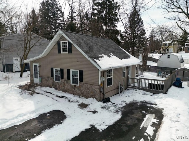 exterior space featuring stone siding, roof with shingles, and a deck