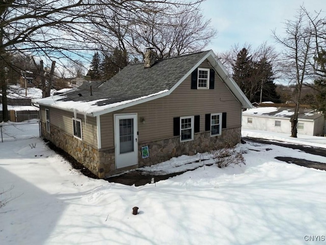 view of front of property featuring stone siding, a shingled roof, a chimney, and fence