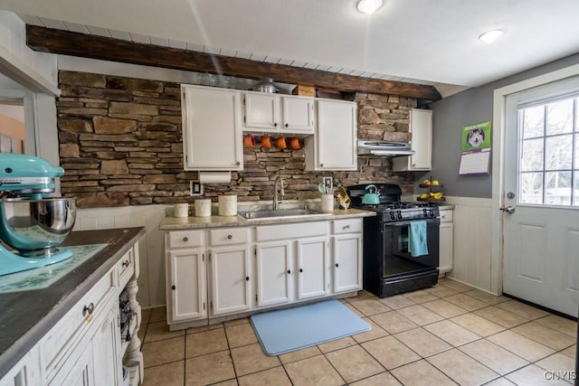 kitchen featuring black gas range, white cabinets, a wainscoted wall, under cabinet range hood, and a sink