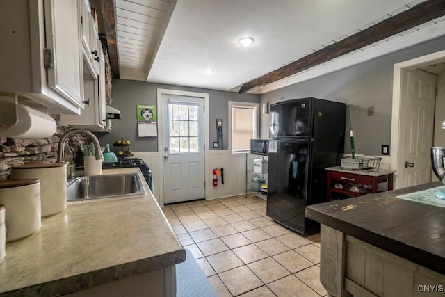 kitchen with black appliances, wainscoting, a sink, and beam ceiling