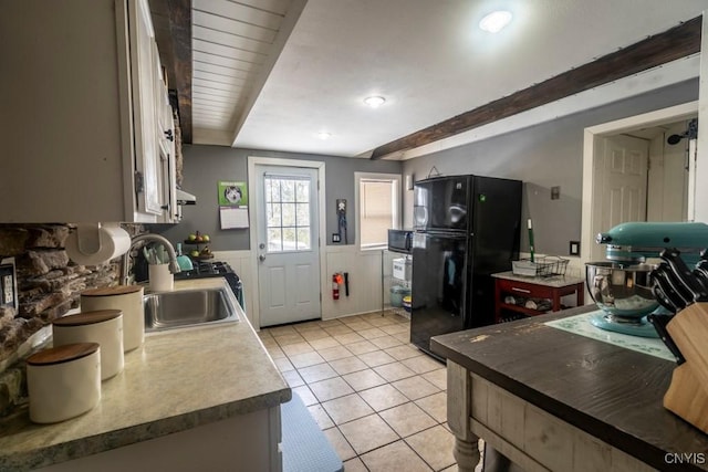 kitchen featuring light tile patterned floors, a wainscoted wall, a sink, freestanding refrigerator, and beamed ceiling