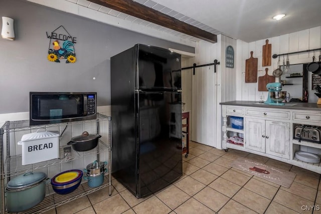 kitchen with a barn door, dark countertops, beamed ceiling, freestanding refrigerator, and light tile patterned flooring