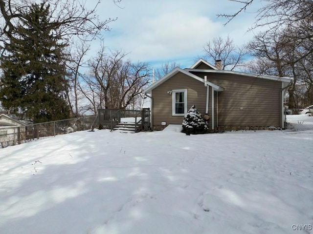 snow covered property featuring a deck, a chimney, and fence