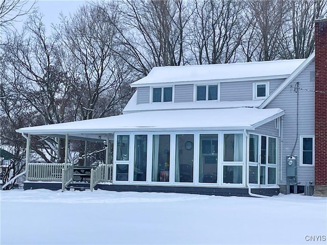 snow covered property with a chimney and a sunroom