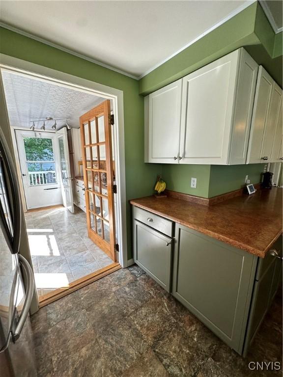 kitchen with french doors, dark countertops, freestanding refrigerator, stone finish flooring, and white cabinetry