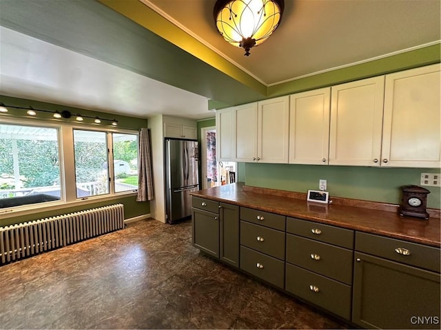 kitchen featuring dark countertops, radiator, ornamental molding, freestanding refrigerator, and white cabinets