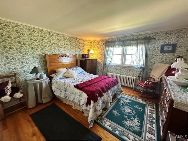 bedroom featuring radiator, wallpapered walls, ornamental molding, and wood finished floors