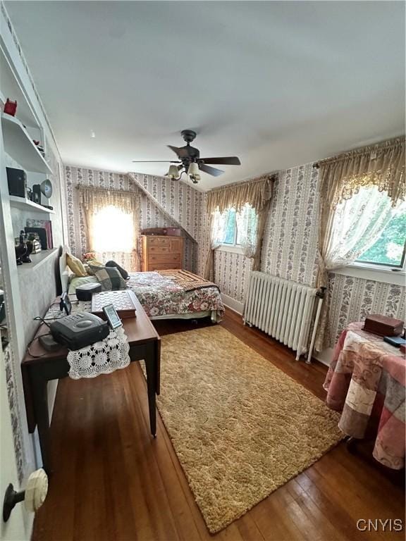 bedroom with ceiling fan, radiator, wood-type flooring, and wallpapered walls