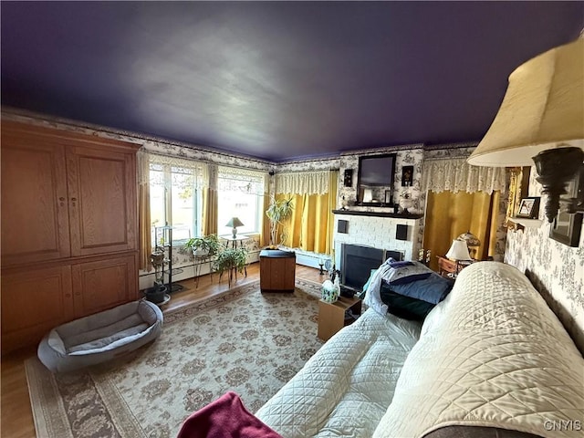 living room featuring a large fireplace, baseboard heating, wallpapered walls, and wood finished floors