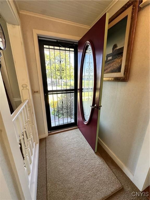 doorway featuring baseboards, ornamental molding, and carpet flooring