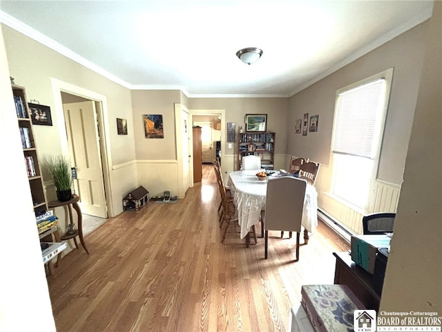 dining room featuring a baseboard heating unit, a wainscoted wall, crown molding, and light wood finished floors