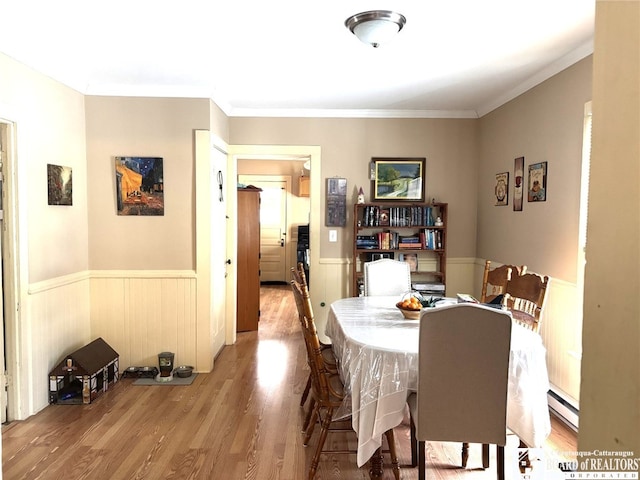 dining area with a baseboard radiator, a wainscoted wall, crown molding, and wood finished floors