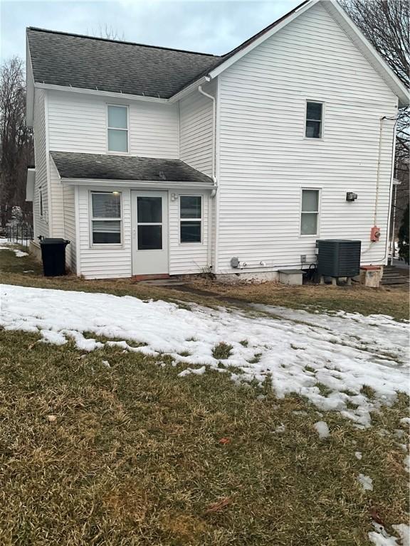 snow covered rear of property featuring a shingled roof and cooling unit