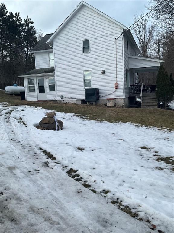 snow covered back of property featuring covered porch and cooling unit