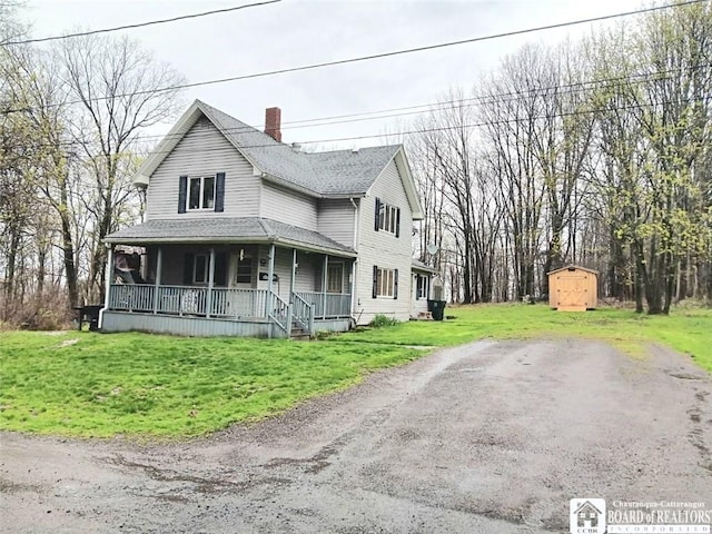 farmhouse-style home featuring an outbuilding, covered porch, a storage unit, a front lawn, and a chimney