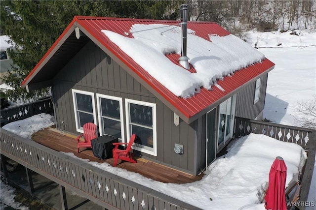 snow covered house featuring a deck and board and batten siding