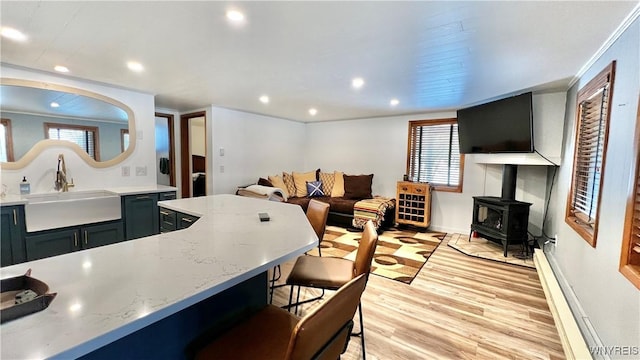 kitchen featuring light wood finished floors, a wood stove, a kitchen bar, a sink, and recessed lighting