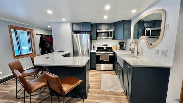 kitchen with light wood finished floors, a breakfast bar area, recessed lighting, appliances with stainless steel finishes, and a sink