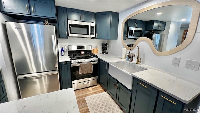 kitchen featuring arched walkways, stainless steel appliances, a sink, light wood-type flooring, and light stone countertops